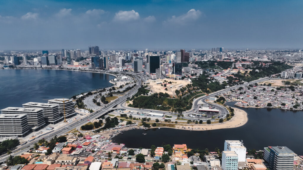 The cityscape of Luanda showcases a blend of modern buildings, coastal areas, and busy streets under a clear blue sky.